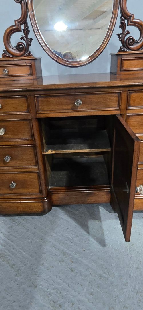 A Victorian mahogany dressing table featuring a central oval swivelling mirror, carved scroll supports, small upper trinket drawers, and twin drawer pedestals flanking a central cupboard. View VIII