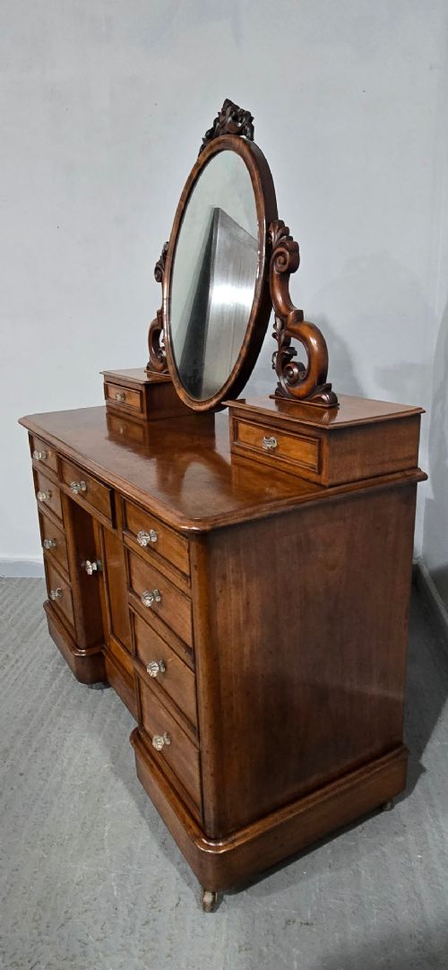A Victorian mahogany dressing table featuring a central oval swivelling mirror, carved scroll supports, small upper trinket drawers, and twin drawer pedestals flanking a central cupboard. View X