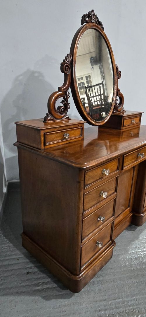 A Victorian mahogany dressing table featuring a central oval swivelling mirror, carved scroll supports, small upper trinket drawers, and twin drawer pedestals flanking a central cupboard. View XI