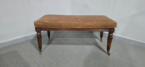 fig 1. A rectangular Regency bench featuring tan leather upholstery, a reeded dark wood frame, tapered carved legs, and brass castors.
