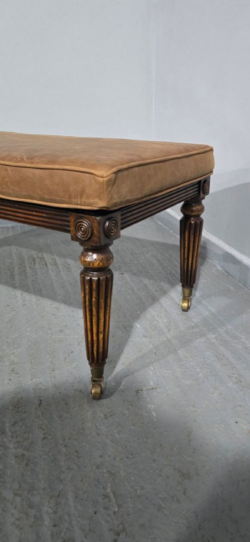 A rectangular Regency bench featuring tan leather upholstery, a reeded dark wood frame, tapered carved legs, and brass castors. View III