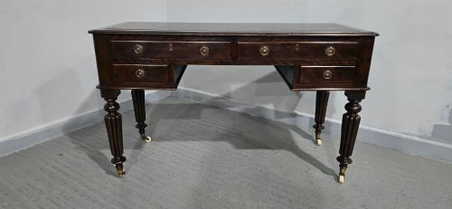 fig 1. A Victorian dark mahogany writing desk featuring a green leather inset top, four drawers with circular brass ring handles, turned fluted legs, and brass castors.