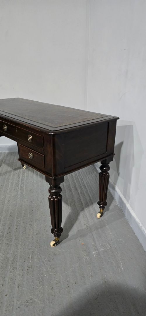A Victorian dark mahogany writing desk featuring a green leather inset top, four drawers with circular brass ring handles, turned fluted legs, and brass castors. View V