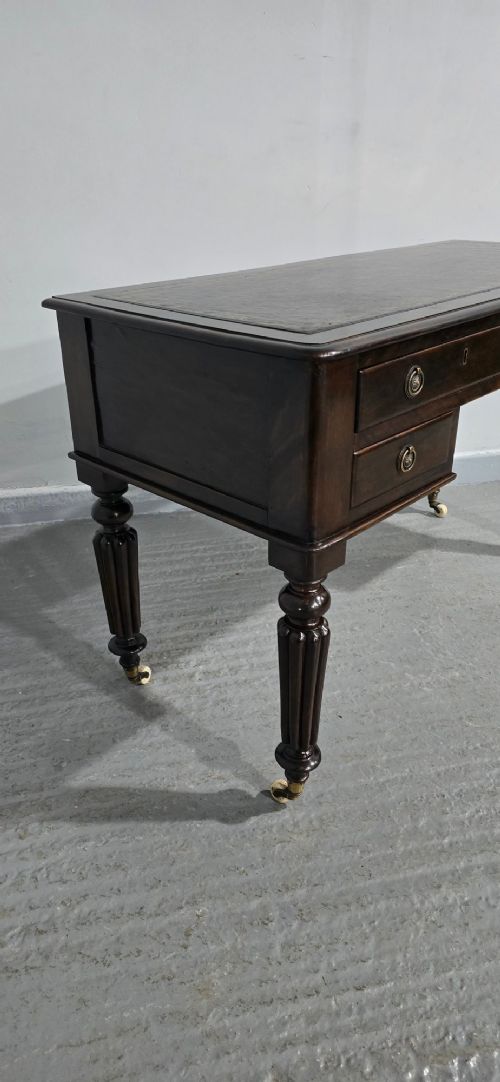 A Victorian dark mahogany writing desk featuring a green leather inset top, four drawers with circular brass ring handles, turned fluted legs, and brass castors. View VI