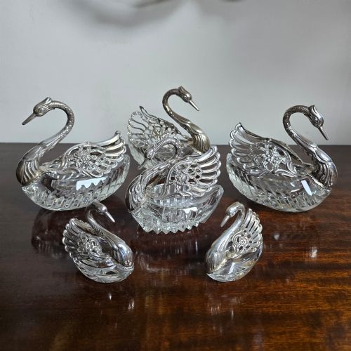 fig 1. A group of cut glass open salt cellars shaped like swans with silver heads and detailed pierced silver wings.