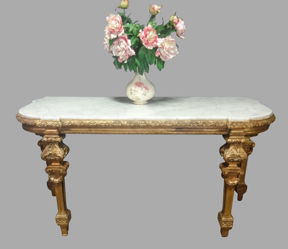 A Regency period giltwood console table featuring carved scroll support legs and a white marble top.