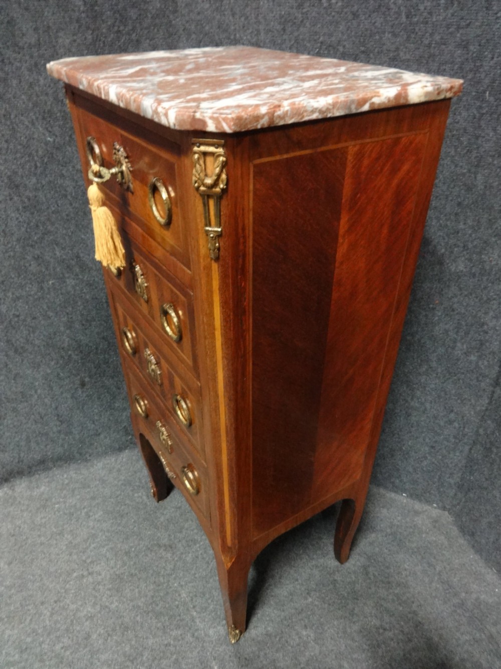 A tall French tulipwood chest featuring four drawers with geometric parquetry inlay, brass ring handles, cabriole legs, and a fitted marble top. View VII