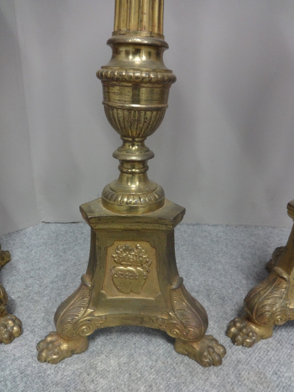 A set of four tall French brass church candlesticks featuring fluted columns, tri-form bases with relief portraits, and claw feet. View III