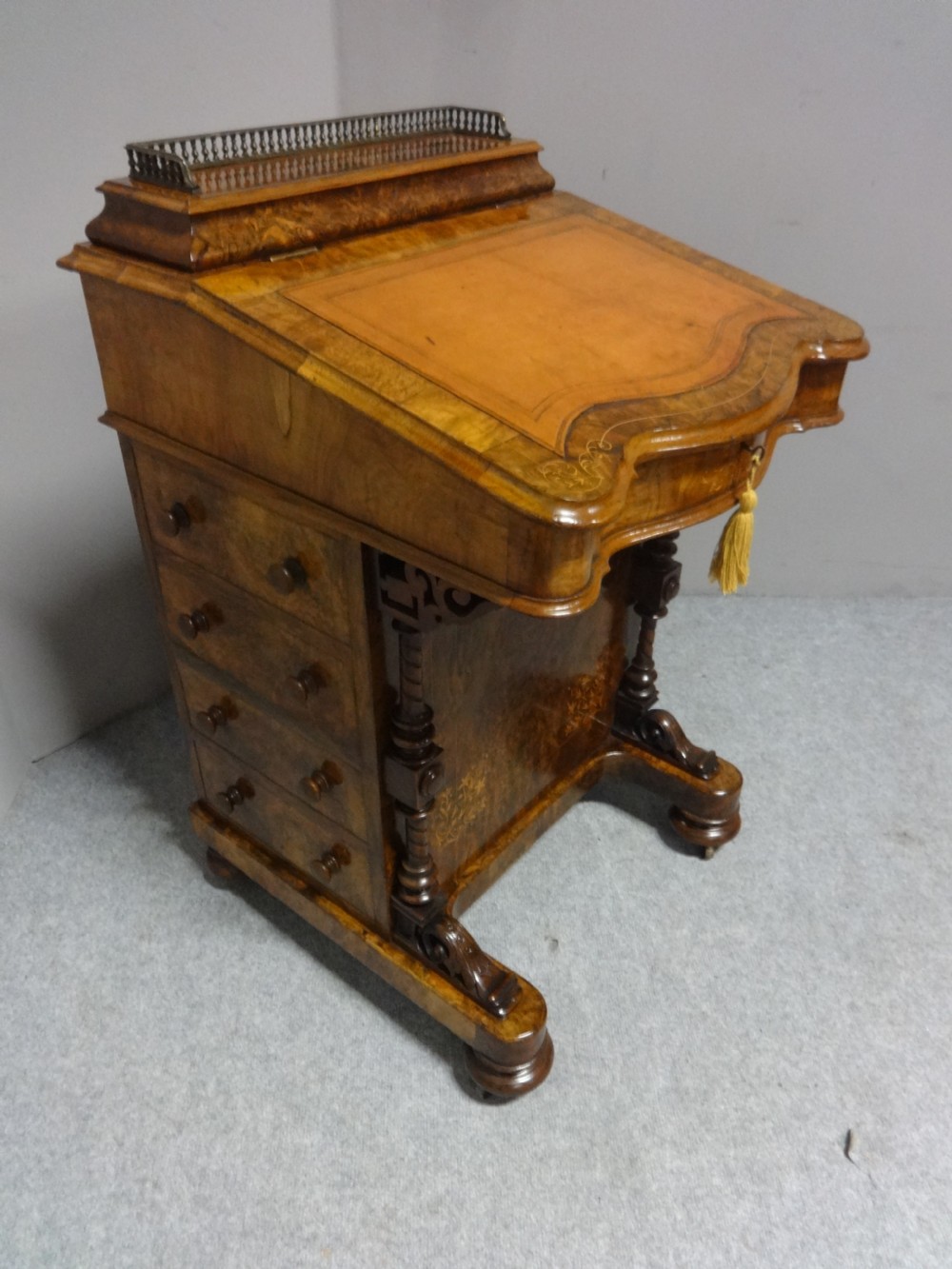 Victorian burr walnut Davenport desk with a gold-tooled leather writing slope, side drawers, intricate marquetry inlay, carved front columns, and a brass gallery rail.