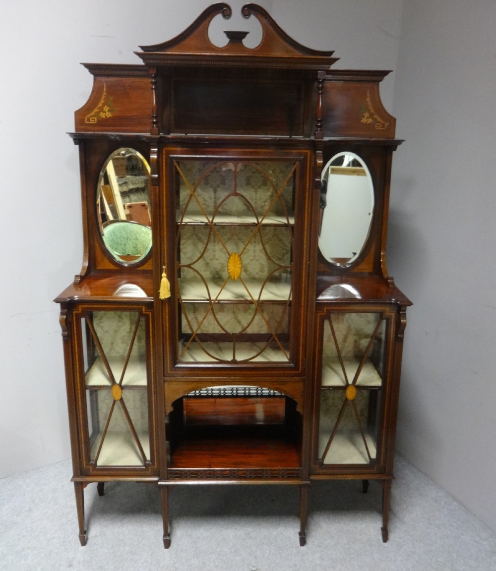 An Edwardian mahogany display cabinet featuring a broken swan-neck pediment, a central glazed door, oval mirrors, and satinwood inlay. View II