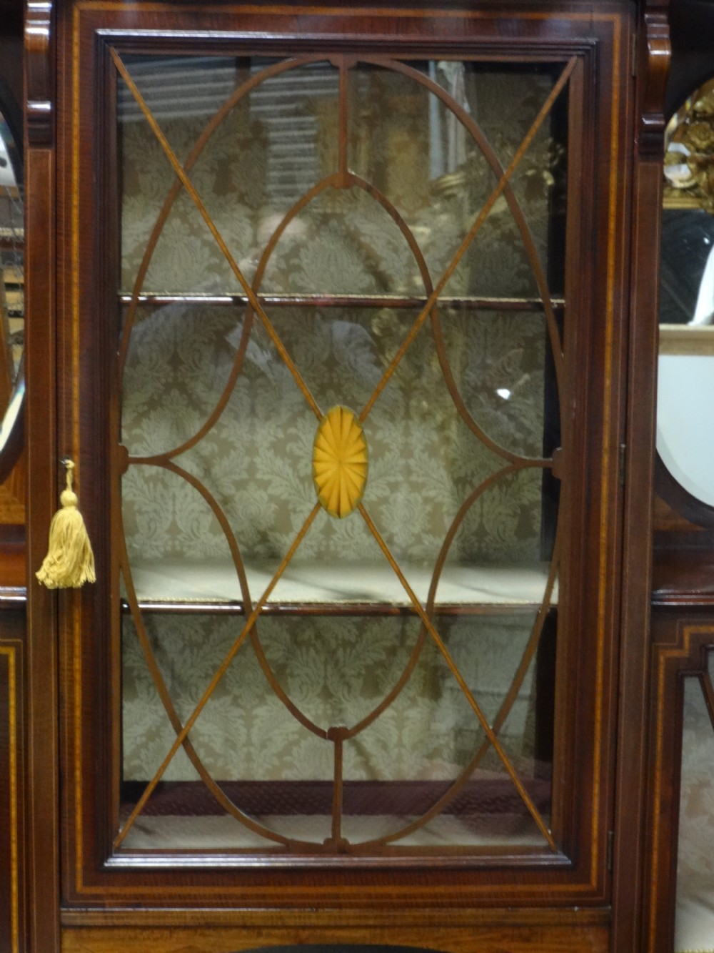 An Edwardian mahogany display cabinet featuring a broken swan-neck pediment, a central glazed door, oval mirrors, and satinwood inlay. View III