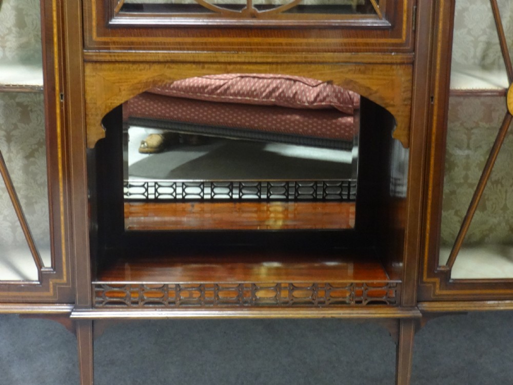 An Edwardian mahogany display cabinet featuring a broken swan-neck pediment, a central glazed door, oval mirrors, and satinwood inlay. View V