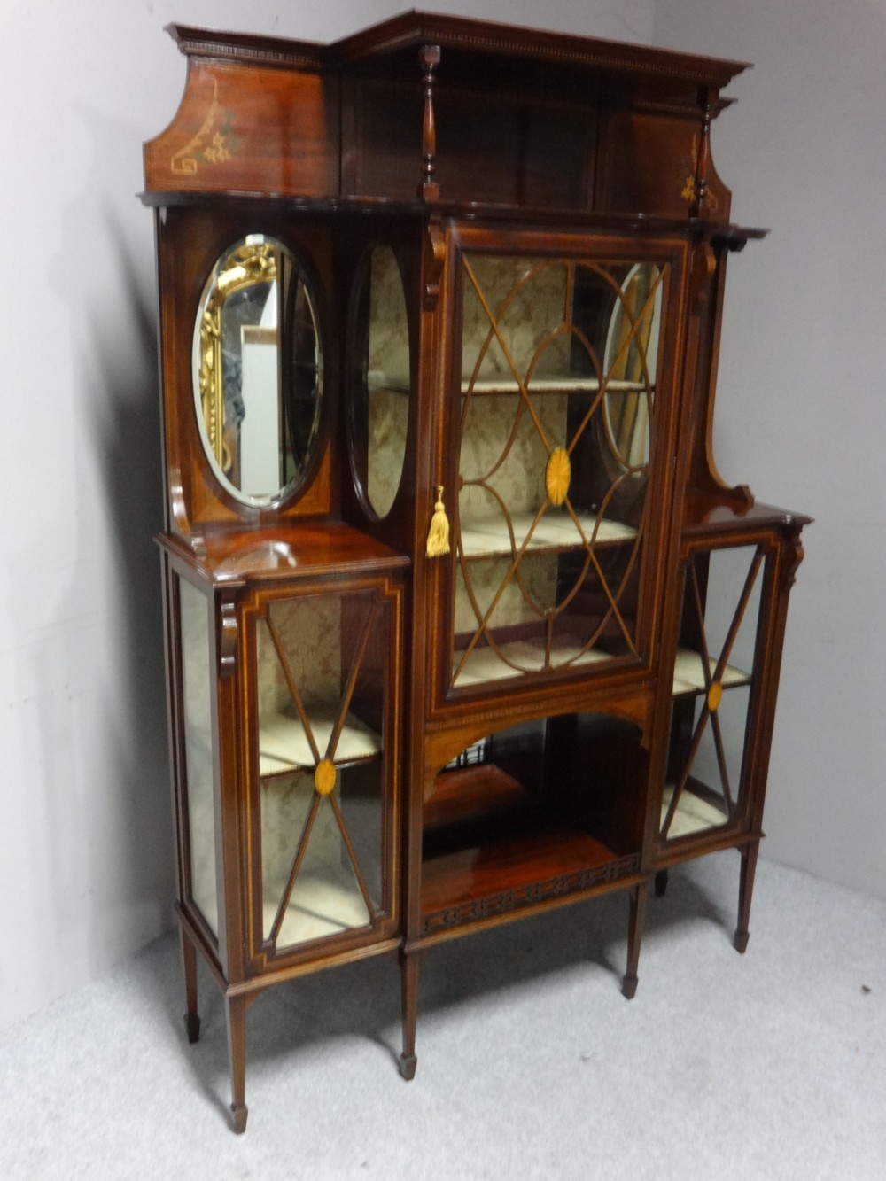 An Edwardian mahogany display cabinet featuring a broken swan-neck pediment, a central glazed door, oval mirrors, and satinwood inlay. View VII