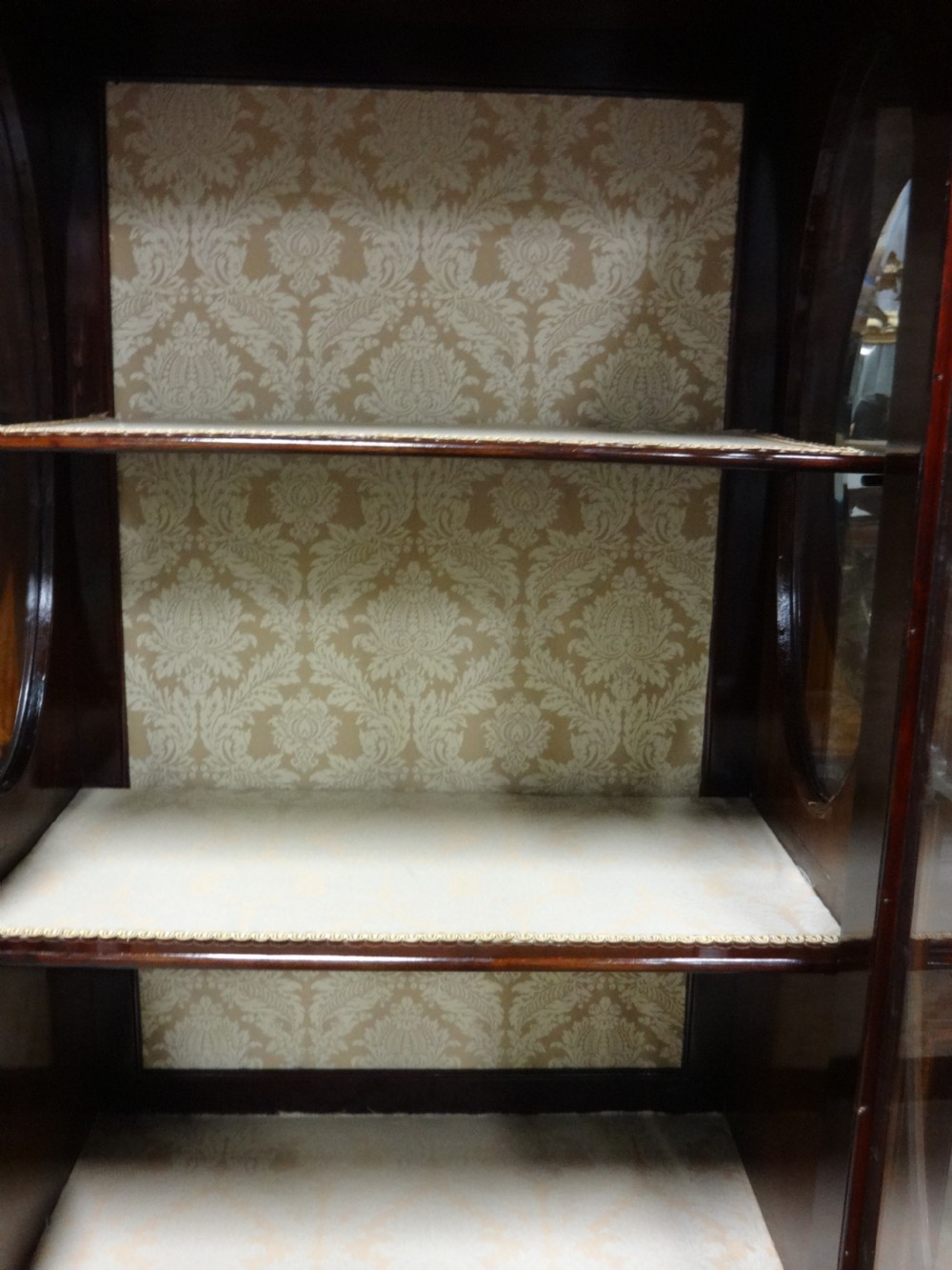 An Edwardian mahogany display cabinet featuring a broken swan-neck pediment, a central glazed door, oval mirrors, and satinwood inlay. View IX