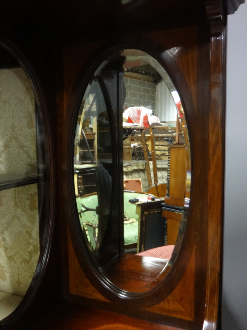 An Edwardian mahogany display cabinet featuring a broken swan-neck pediment, a central glazed door, oval mirrors, and satinwood inlay. View X