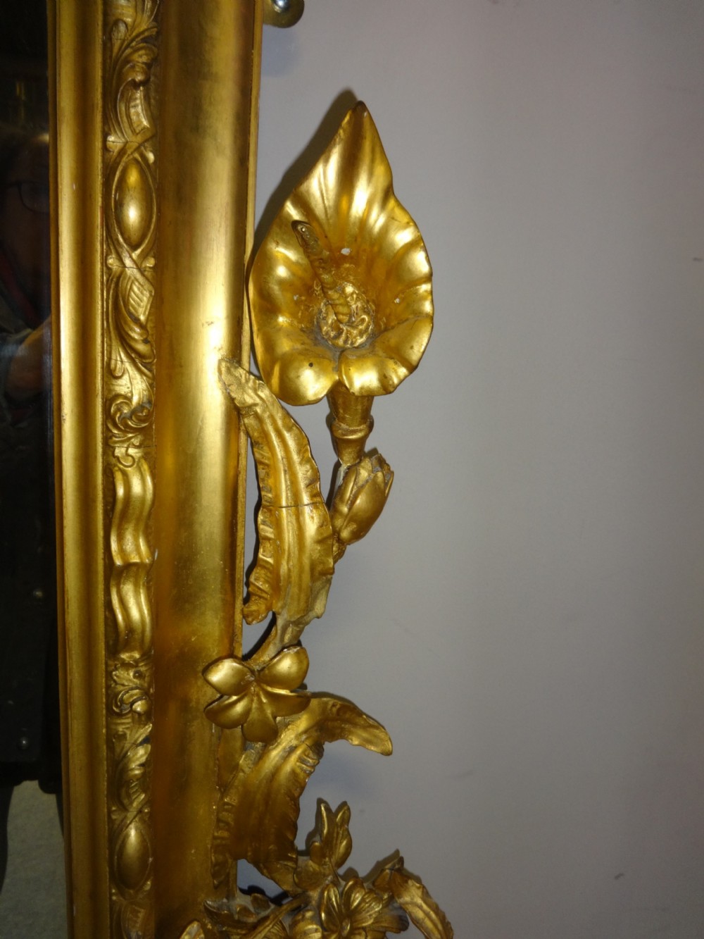 An ornate Victorian giltwood overmantel mirror featuring detailed floral cresting, cherub figures, and a black-topped console shelf supported by scroll brackets. View V