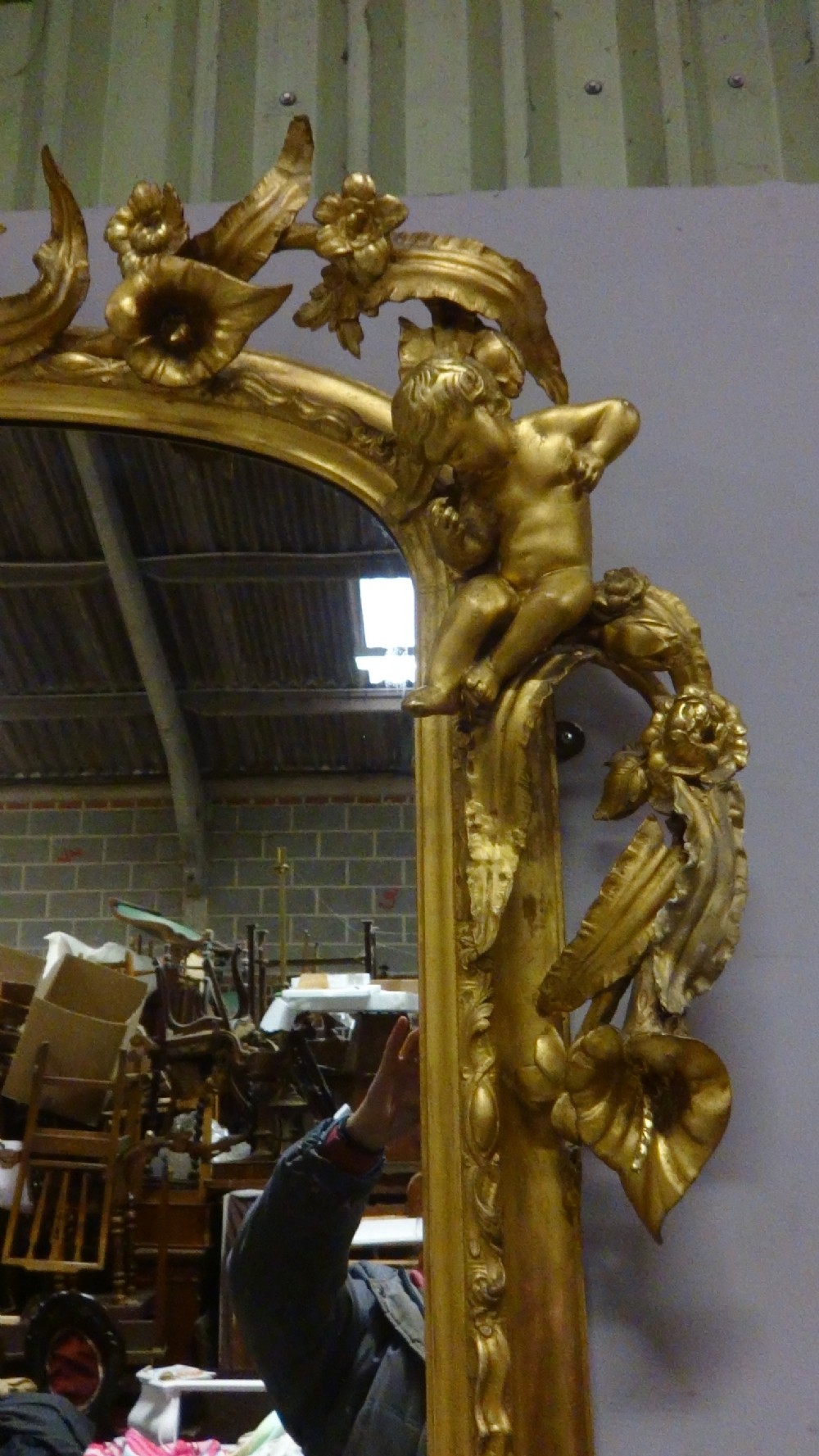 An ornate Victorian giltwood overmantel mirror featuring detailed floral cresting, cherub figures, and a black-topped console shelf supported by scroll brackets. View VIII