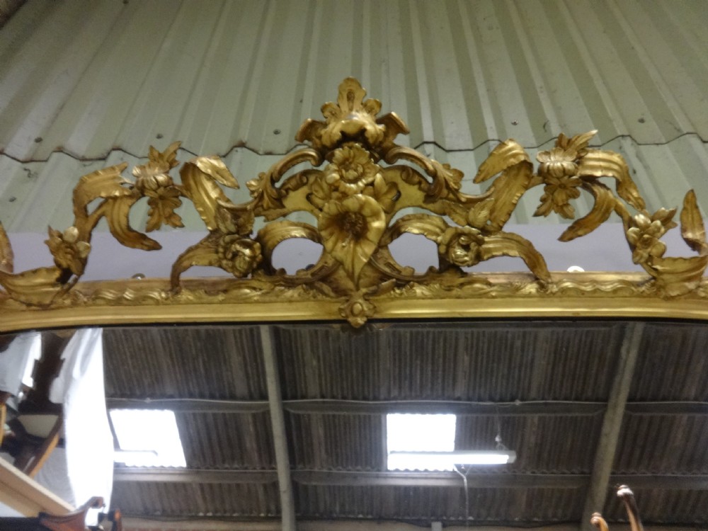 An ornate Victorian giltwood overmantel mirror featuring detailed floral cresting, cherub figures, and a black-topped console shelf supported by scroll brackets. View X