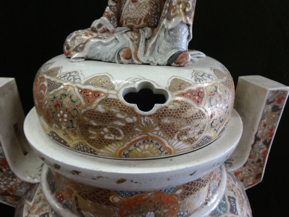 An antique Japanese Satsuma ceramic koro incense burner featuring tripodic legs, side handles, hand-painted figures, gold embellishments, and a seated figure finial on the lid. View III
