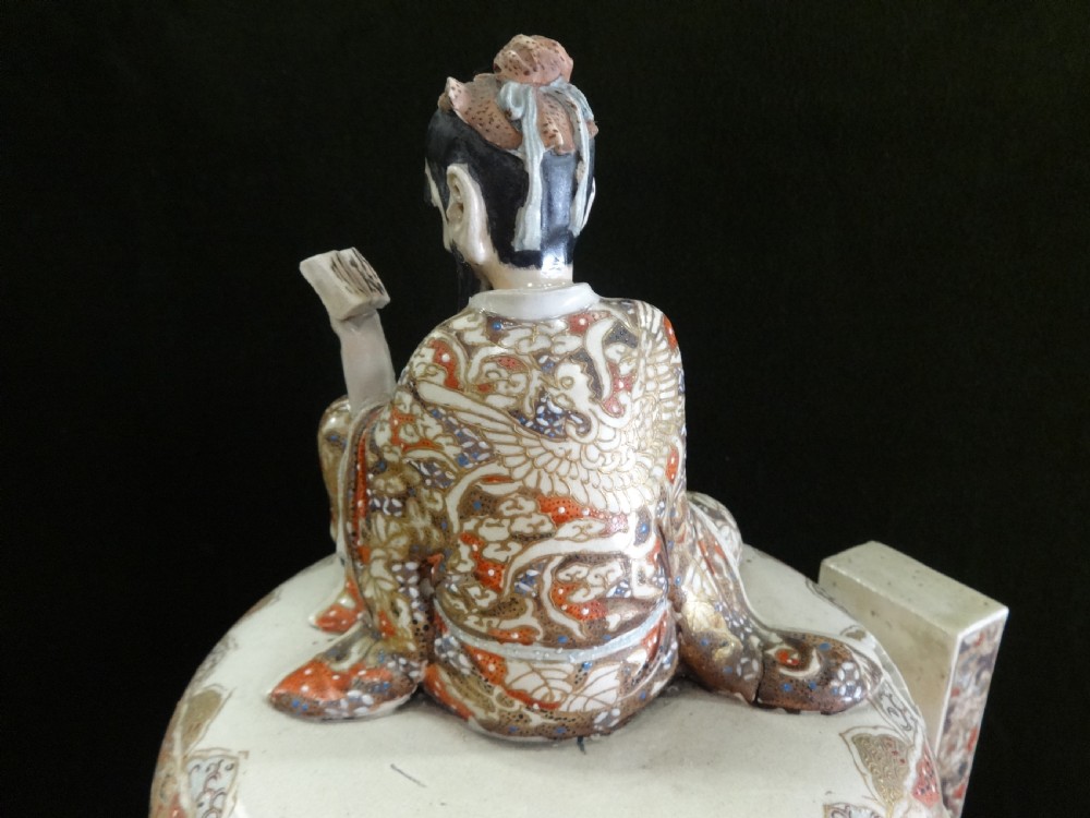 An antique Japanese Satsuma ceramic koro incense burner featuring tripodic legs, side handles, hand-painted figures, gold embellishments, and a seated figure finial on the lid. View XII