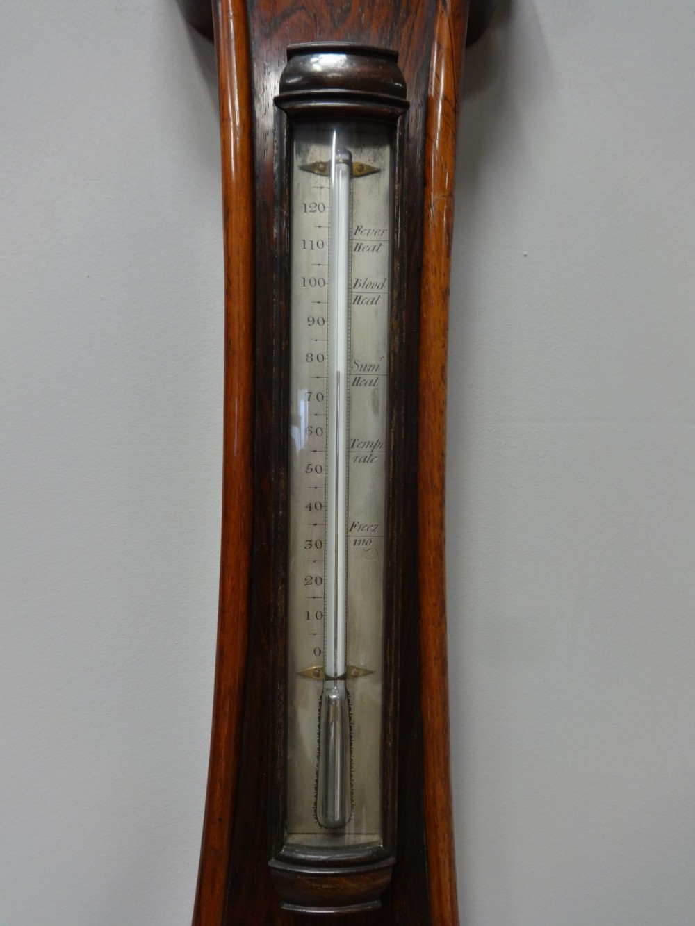 A nineteenth-century rosewood wheel mercury barometer with a brass-trimmed silvered dial and an integrated thermometer tube. View II