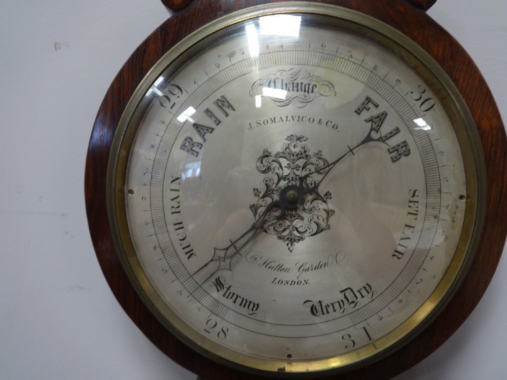 A nineteenth-century rosewood wheel mercury barometer with a brass-trimmed silvered dial and an integrated thermometer tube. View III