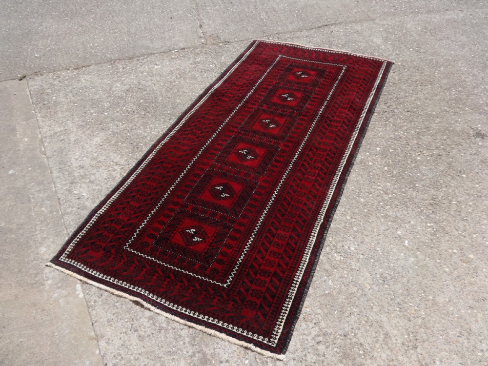 A rectangular hand-knotted wool runner rug with a deep red ground, geometric square medallions, and dark patterned borders.