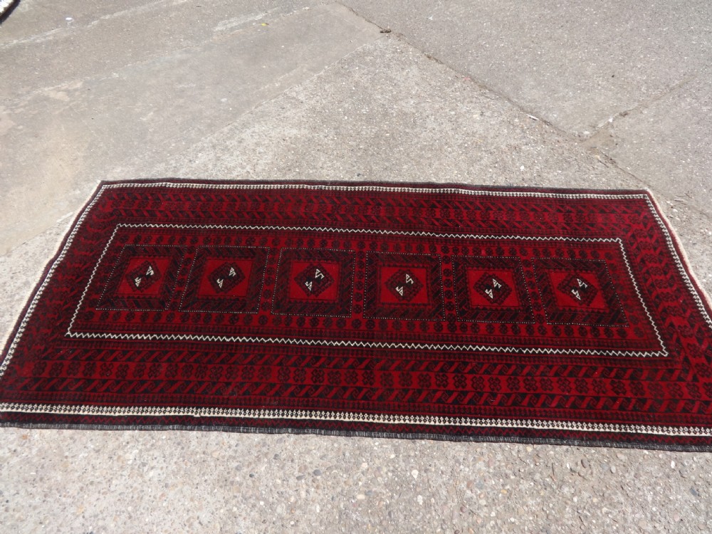 A rectangular hand-knotted wool runner rug with a deep red ground, geometric square medallions, and dark patterned borders. View II
