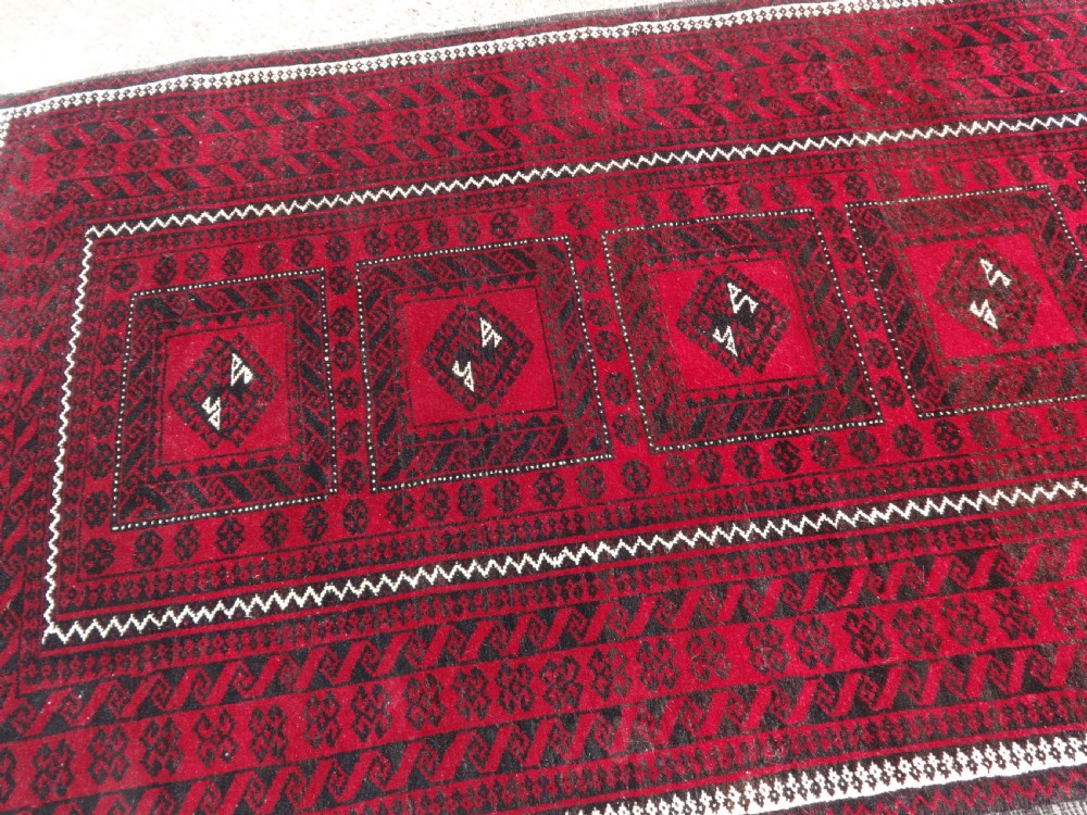 A rectangular hand-knotted wool runner rug with a deep red ground, geometric square medallions, and dark patterned borders. View III