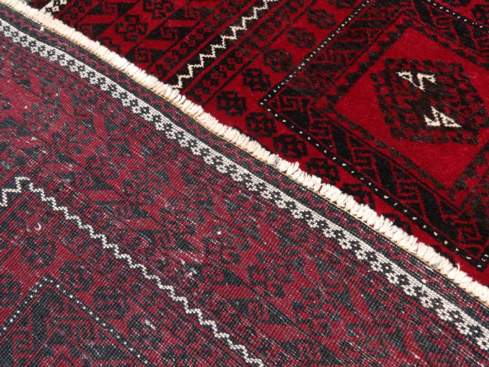 A rectangular hand-knotted wool runner rug with a deep red ground, geometric square medallions, and dark patterned borders. View V