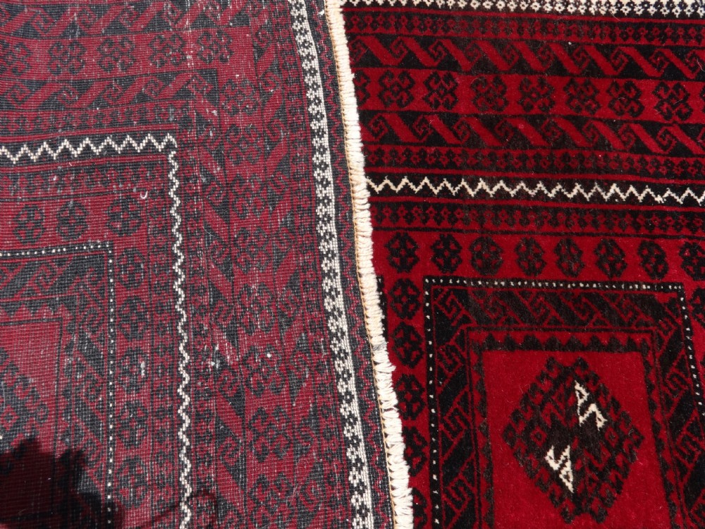 A rectangular hand-knotted wool runner rug with a deep red ground, geometric square medallions, and dark patterned borders. View VI