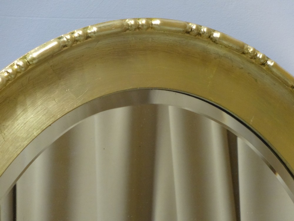 An oval Edwardian wall mirror with a gilded frame featuring beaded trim details around a bevelled glass mirror plate. View VII