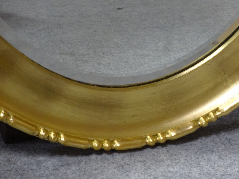 An oval Edwardian wall mirror with a gilded frame featuring beaded trim details around a bevelled glass mirror plate. View VIII