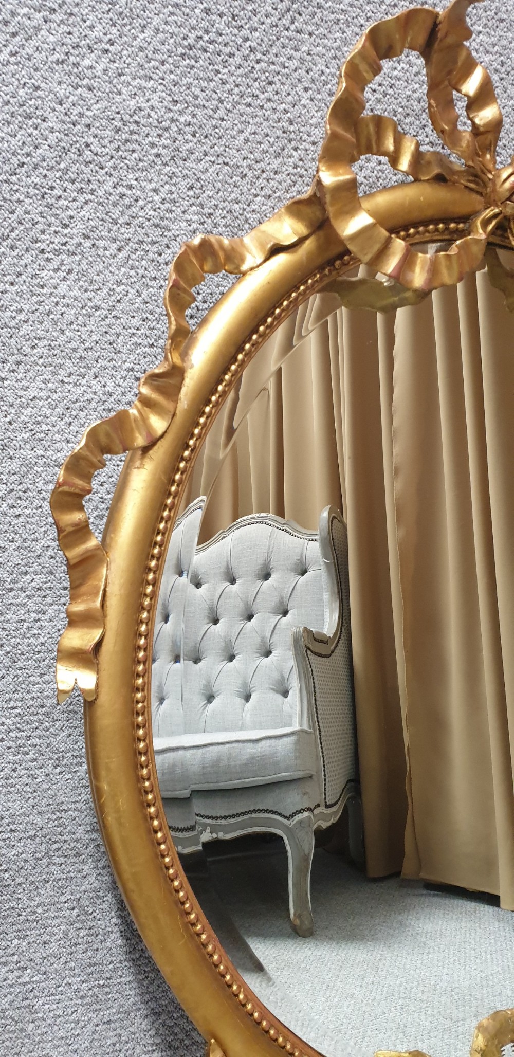 An oval giltwood wall mirror featuring carved ribbon bow detailing at the top and base with a beaded inner rim. View XII