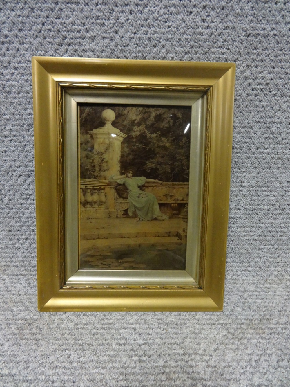 A nineteenth-century convex glass chrystoleum depicting a lady in a green gown sitting on a stone balustrade, set inside a moulded gold frame.