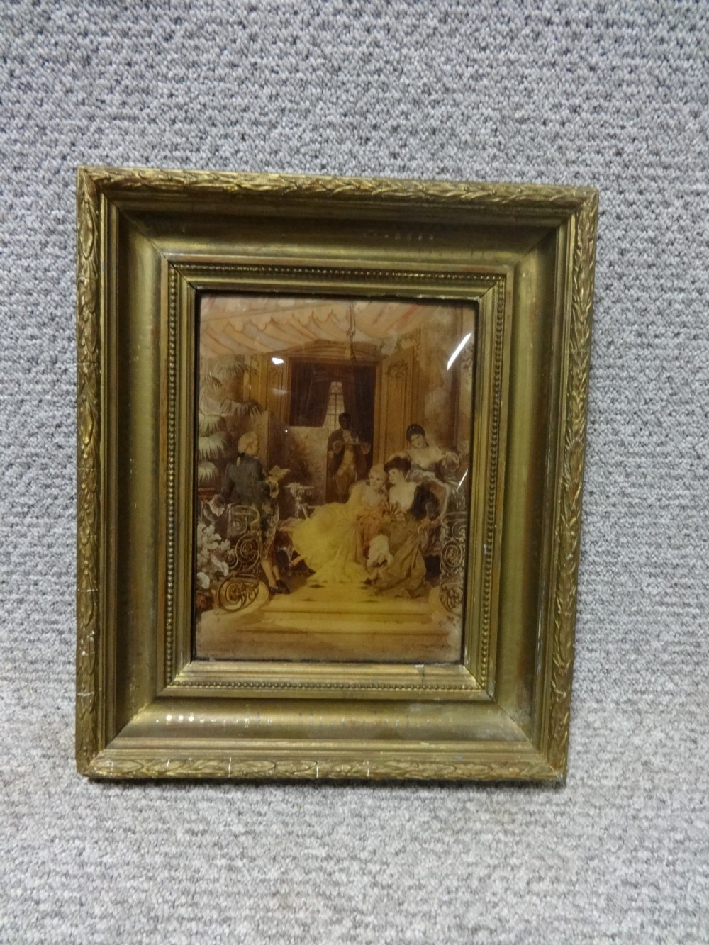 A 19th-century chrystoleum print on convex glass depicting an interior genre scene with figures in classical dress inside an ornate gilt frame.