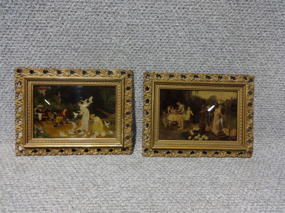 A pair of late 19th-century chrystoleum glass prints depicting romantic garden scenes inside ornate gold gilt frames.