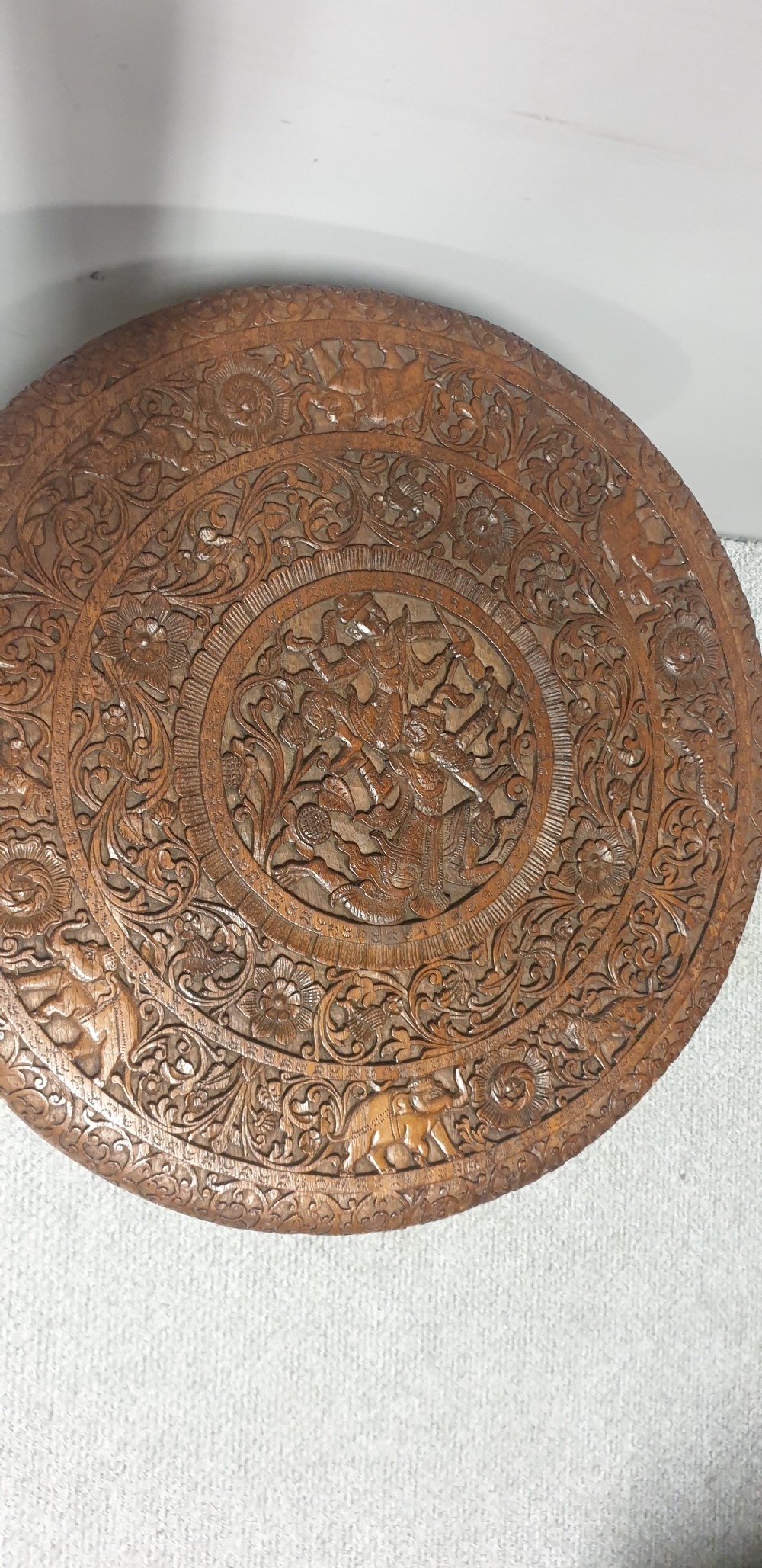 A circular dark wood side table featuring relief foliage carving on top and supported by three sculpted mythological figure legs. View IV