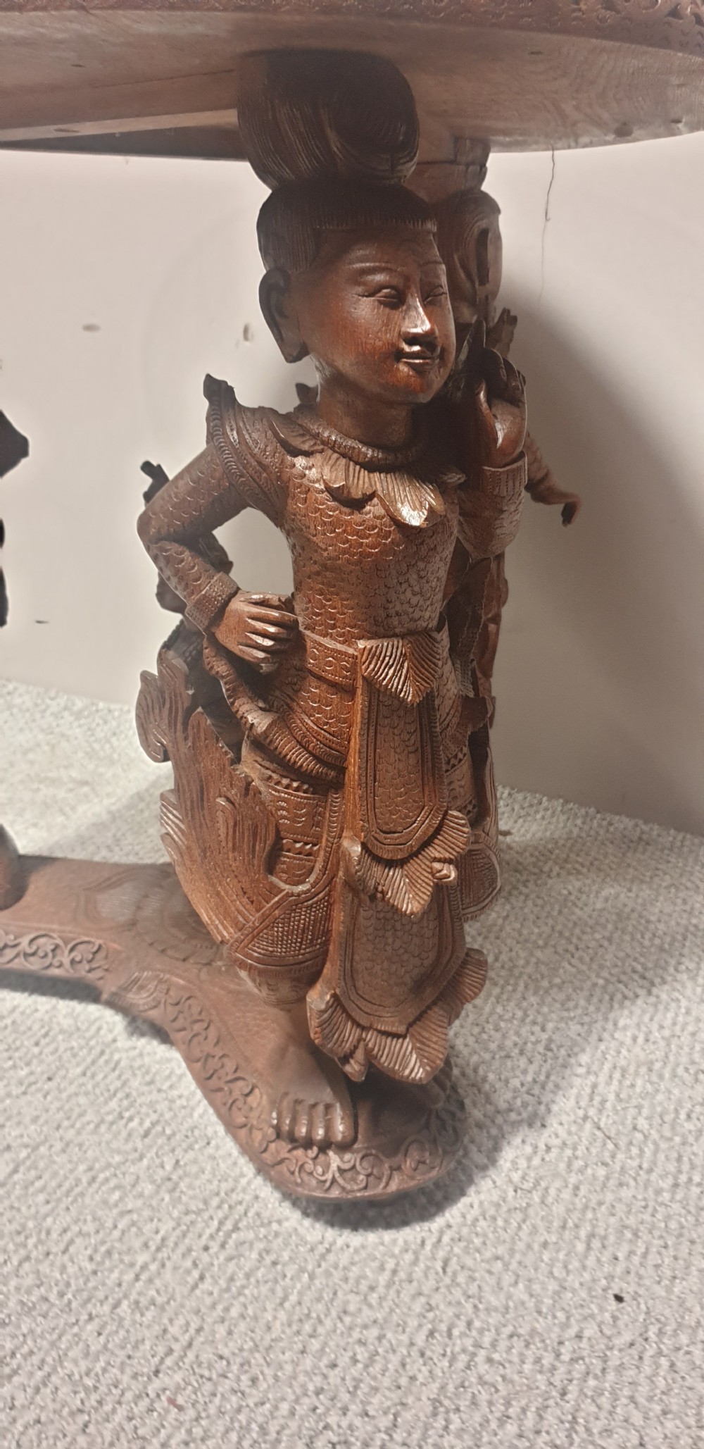 A circular dark wood side table featuring relief foliage carving on top and supported by three sculpted mythological figure legs. View VI