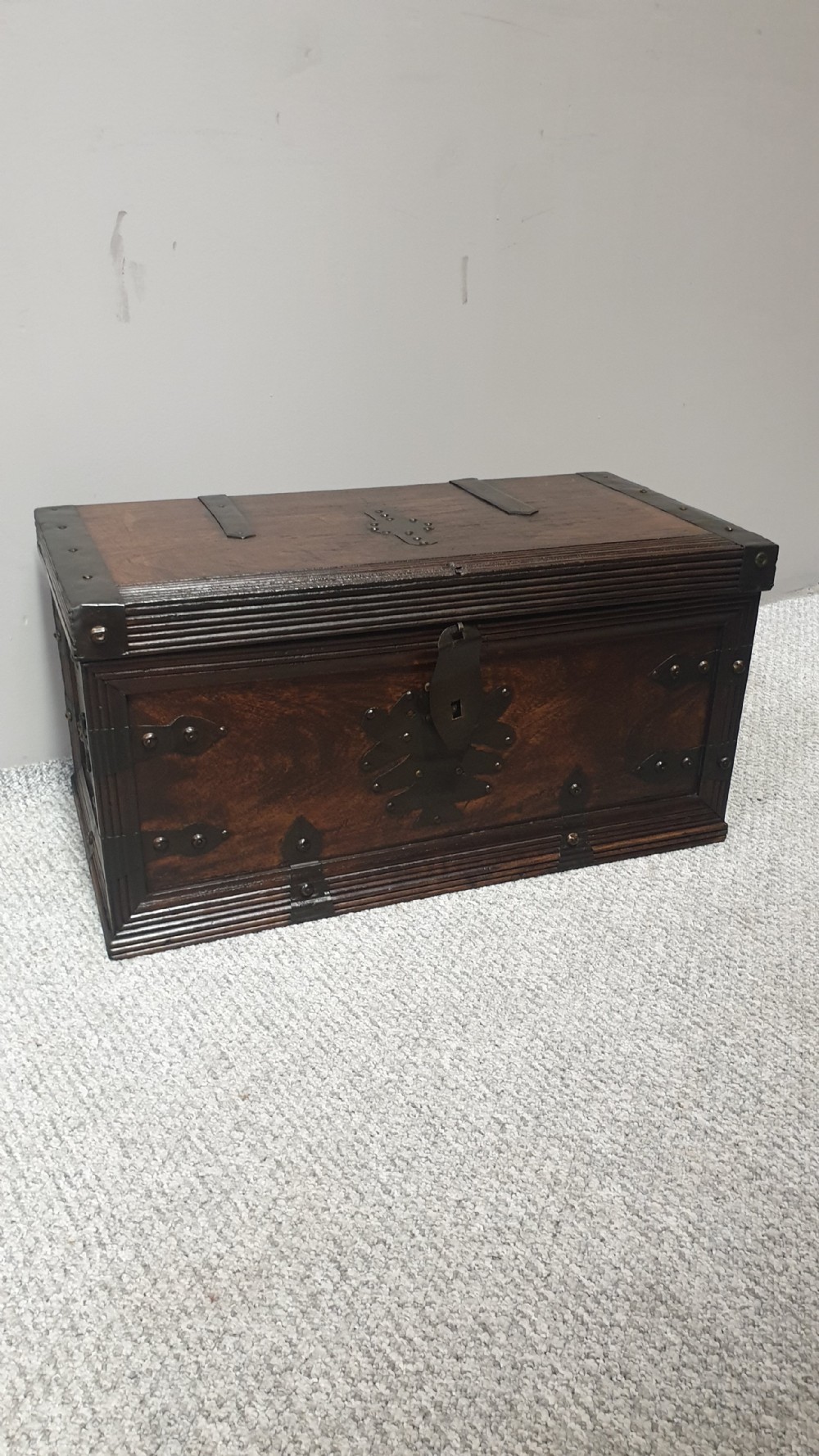 A dark mahogany wooden chest featuring decorative forged iron strapwork, corner brackets, and a central iron escutcheon plate.