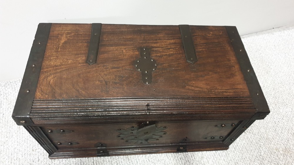A dark mahogany wooden chest featuring decorative forged iron strapwork, corner brackets, and a central iron escutcheon plate. View V