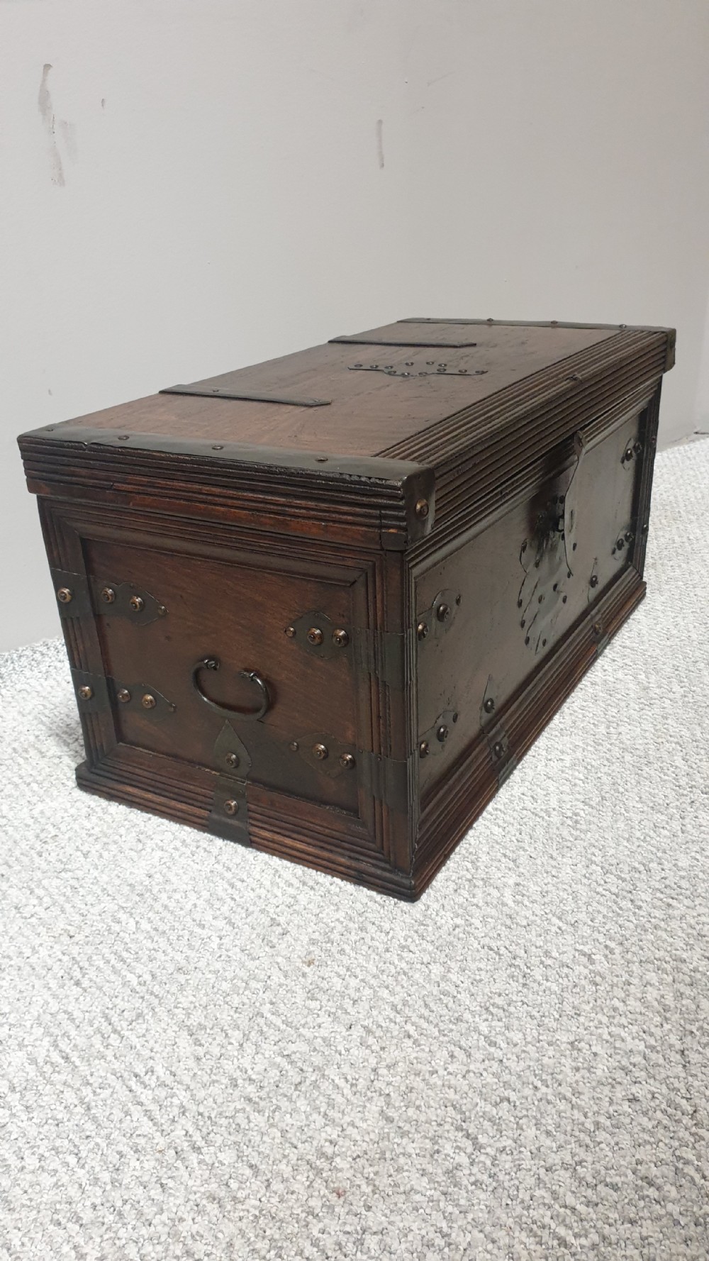 A dark mahogany wooden chest featuring decorative forged iron strapwork, corner brackets, and a central iron escutcheon plate. View VI