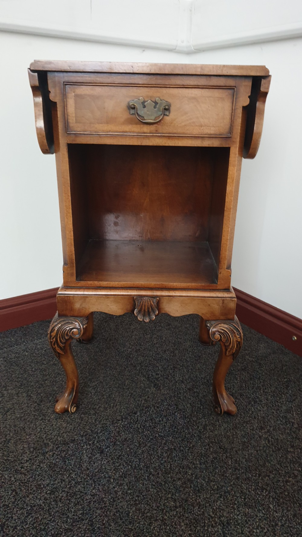 A Queen Anne style walnut bedside cabinet featuring side drop flaps, a single drawer over an open compartment, a carved shell apron, and cabriole legs. View V