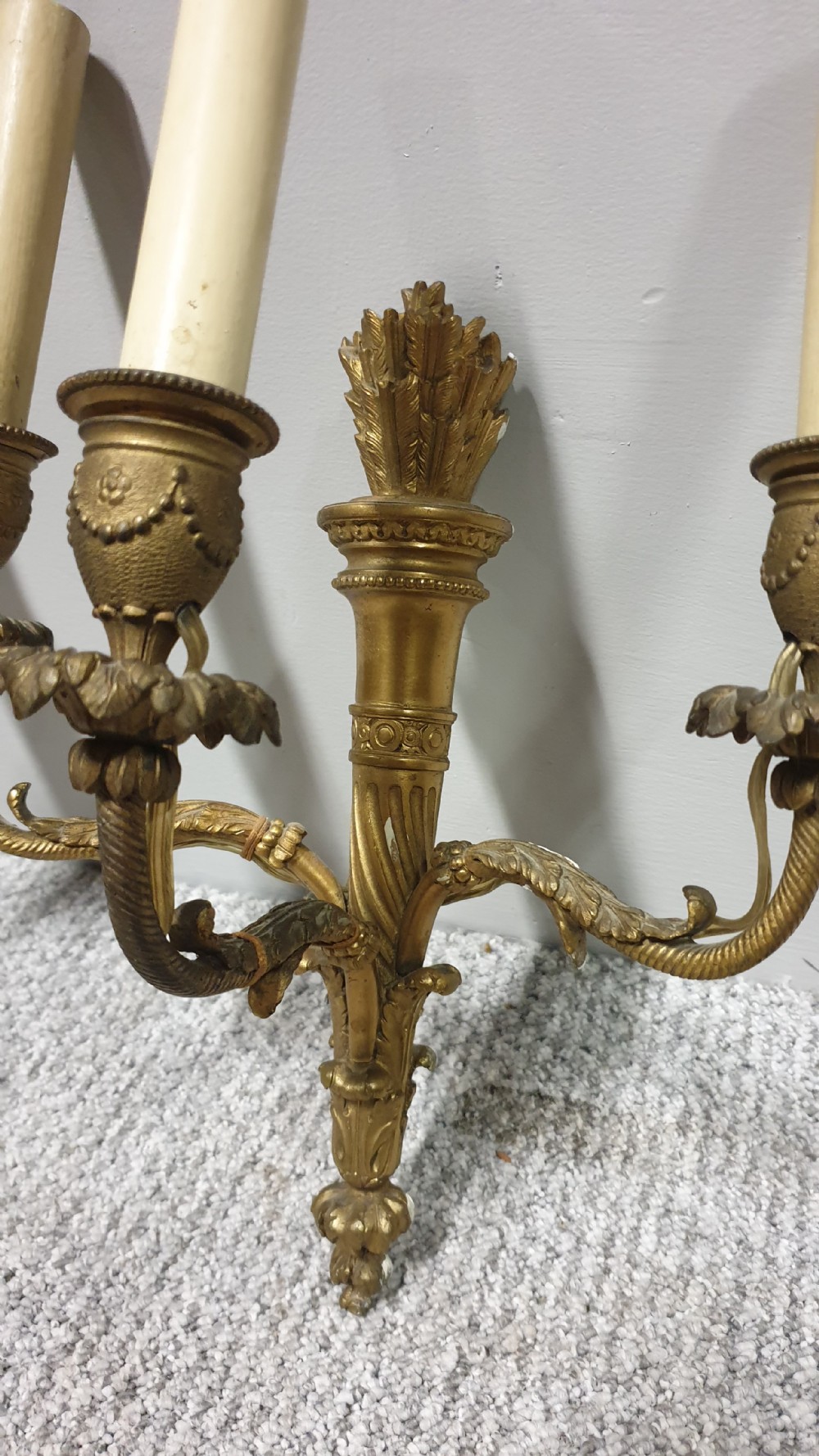 A pair of French Neoclassical gilt brass three-light wall sconces featuring fluted torch backplates, scrolling foliate arms, and cream candle sleeves. View III