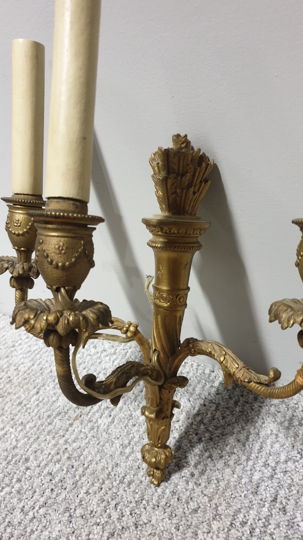A pair of French Neoclassical gilt brass three-light wall sconces featuring fluted torch backplates, scrolling foliate arms, and cream candle sleeves. View IV