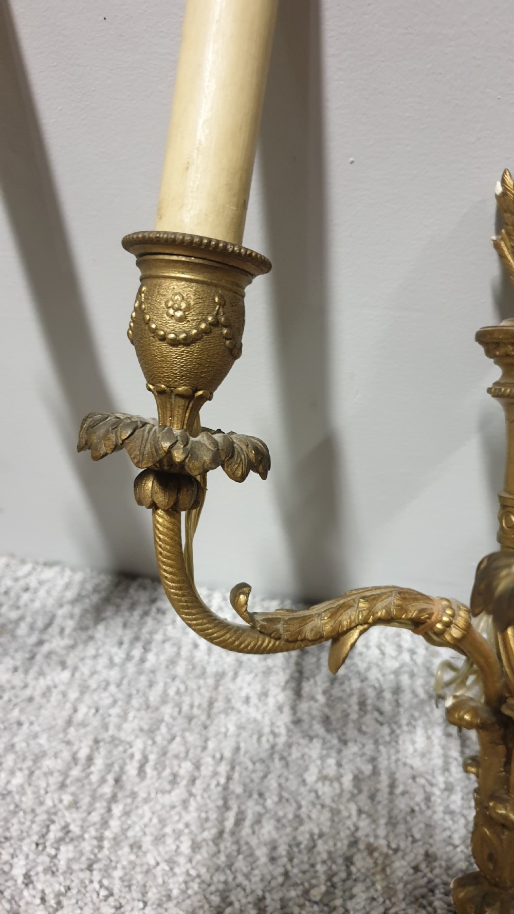 A pair of French Neoclassical gilt brass three-light wall sconces featuring fluted torch backplates, scrolling foliate arms, and cream candle sleeves. View V