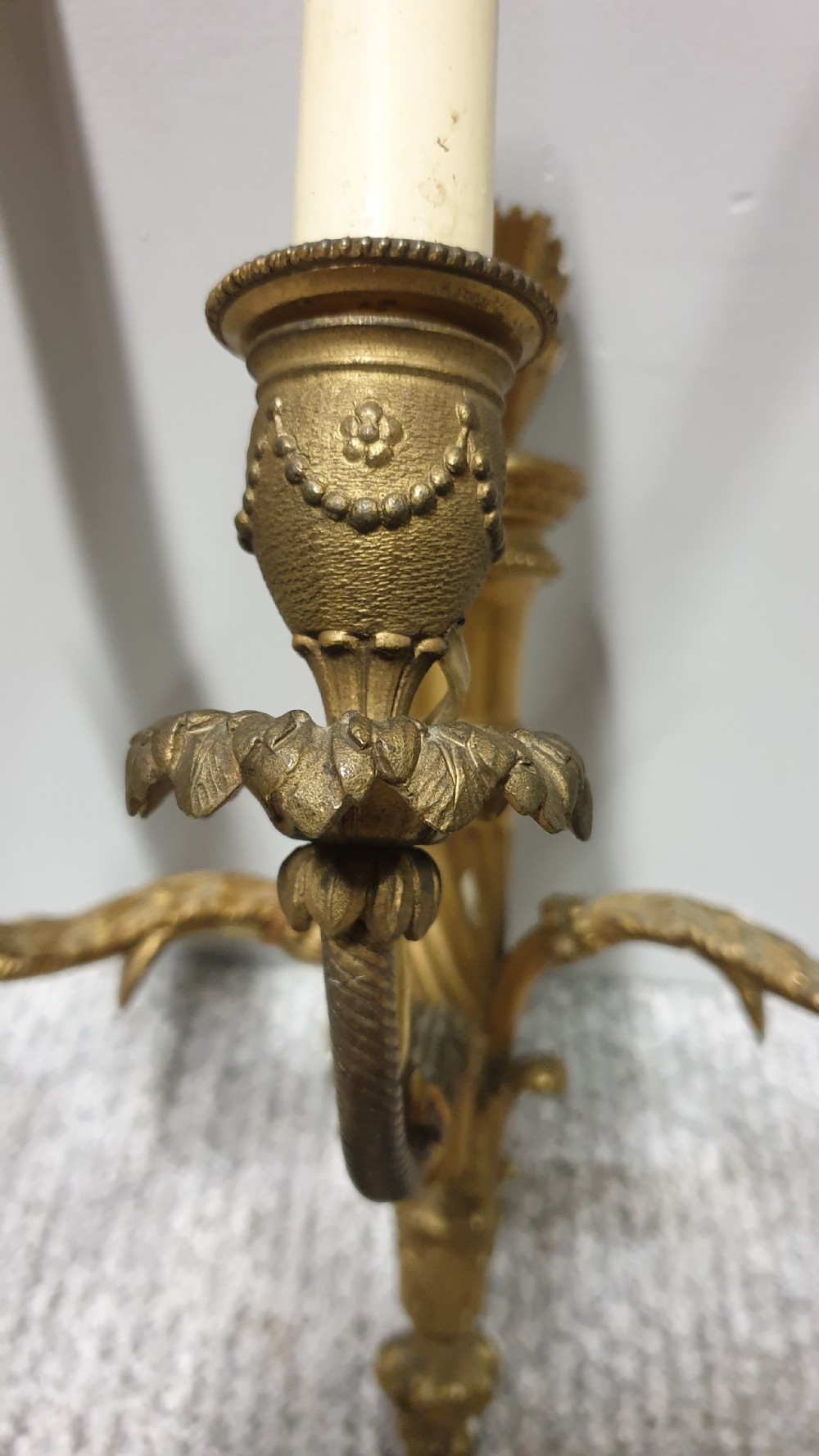 A pair of French Neoclassical gilt brass three-light wall sconces featuring fluted torch backplates, scrolling foliate arms, and cream candle sleeves. View VI