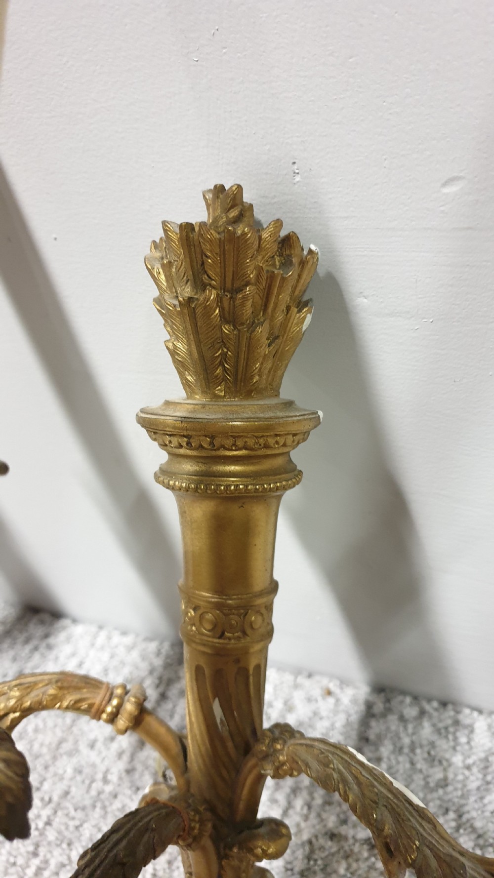 A pair of French Neoclassical gilt brass three-light wall sconces featuring fluted torch backplates, scrolling foliate arms, and cream candle sleeves. View VIII
