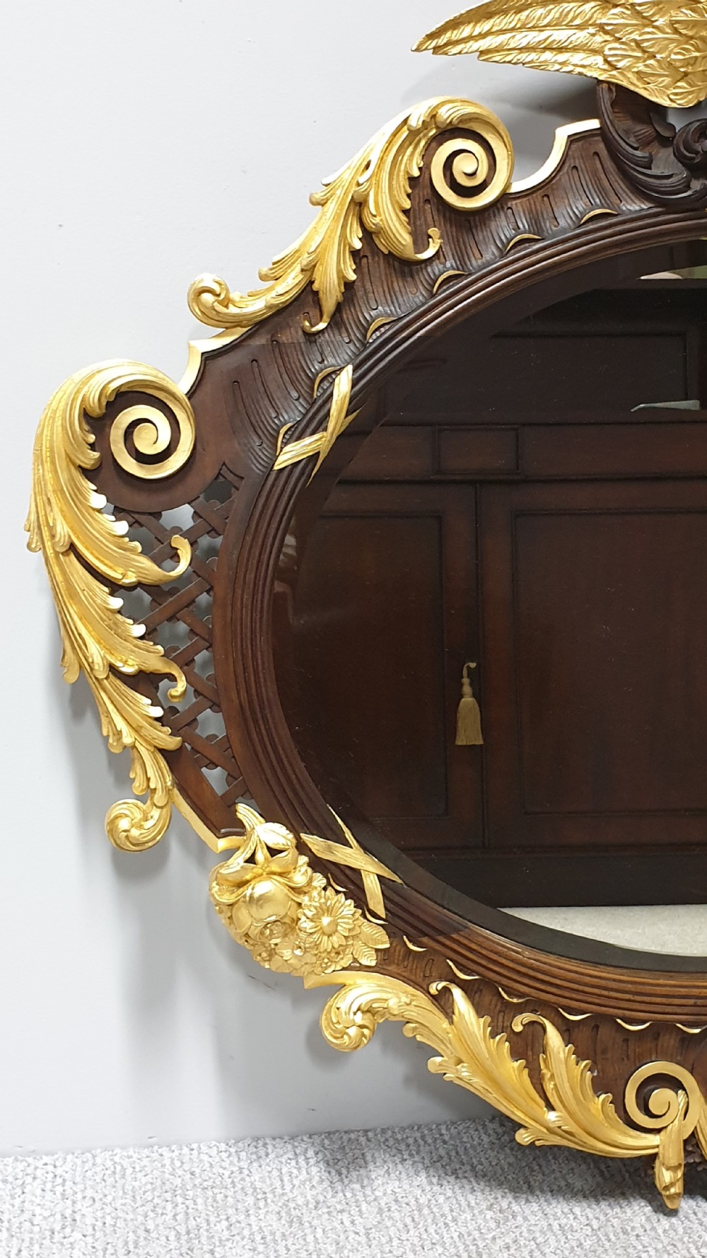 An ornate oval mahogany wall mirror featuring a carved eagle crest, parcel gilt acanthus leaf borders, side lattice panels, and a central classical mask motif at the base. View II