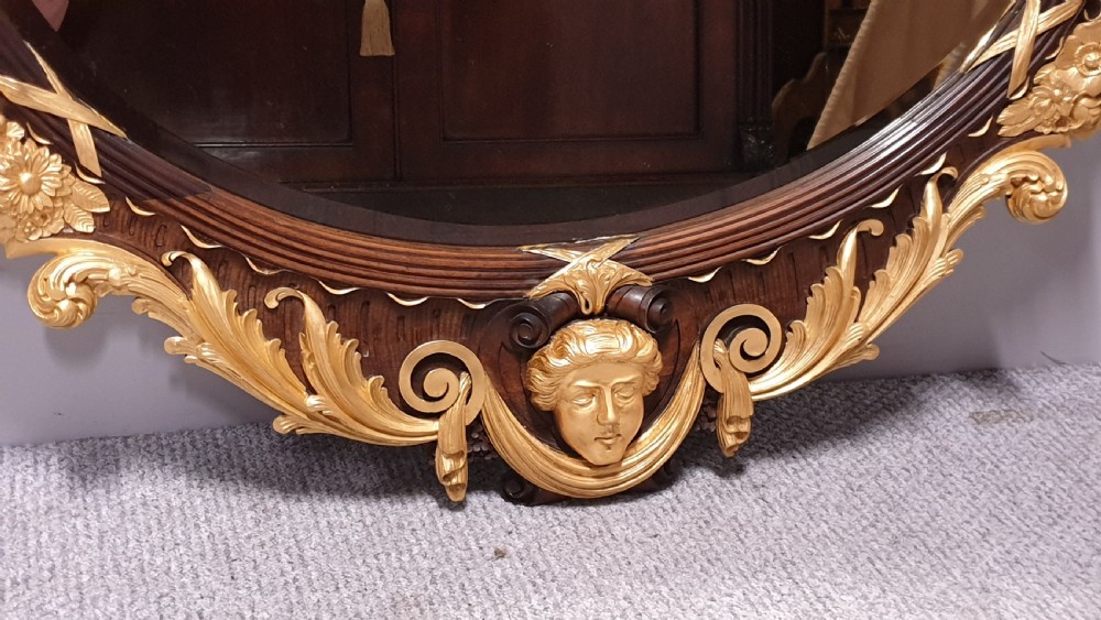 An ornate oval mahogany wall mirror featuring a carved eagle crest, parcel gilt acanthus leaf borders, side lattice panels, and a central classical mask motif at the base. View III